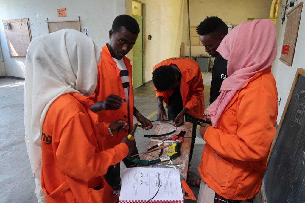 Auszubildende Frauen und Männer in orangen Mänteln arbeiten mit Kabeln