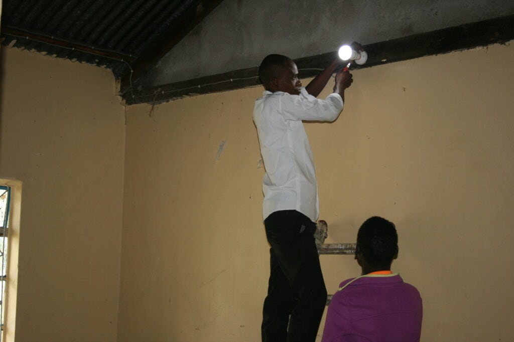 Ein Mann installiert eine Lampe im Rahmen von Solar Learning Kenia eine Lampe in einem Haus