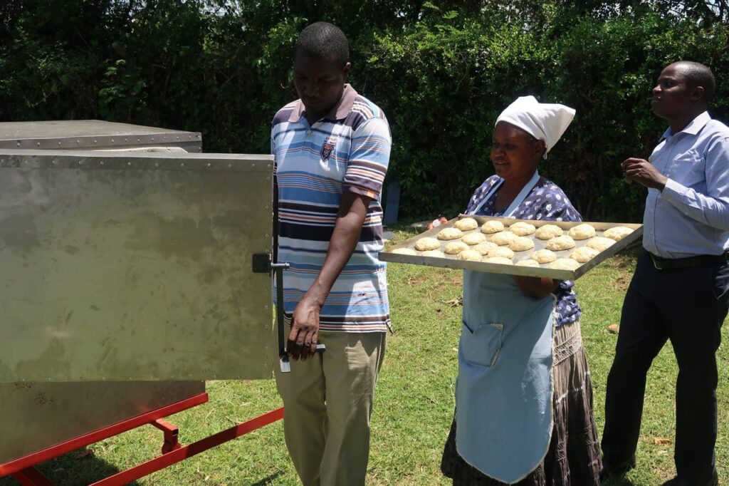 Eine Frau trägt auf einem Blech kleine Brötchen zum Solarofen.