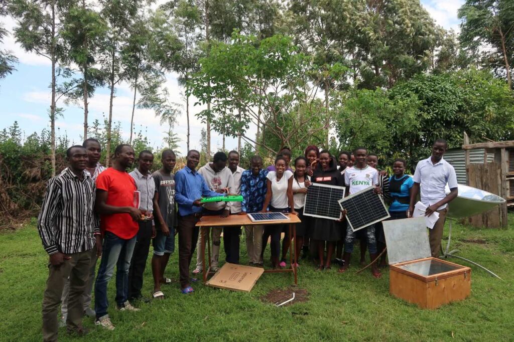 Gruppenbild der 19 Teilnehmenden mit Solarpanels, im Hintergrund hohe Bäume.