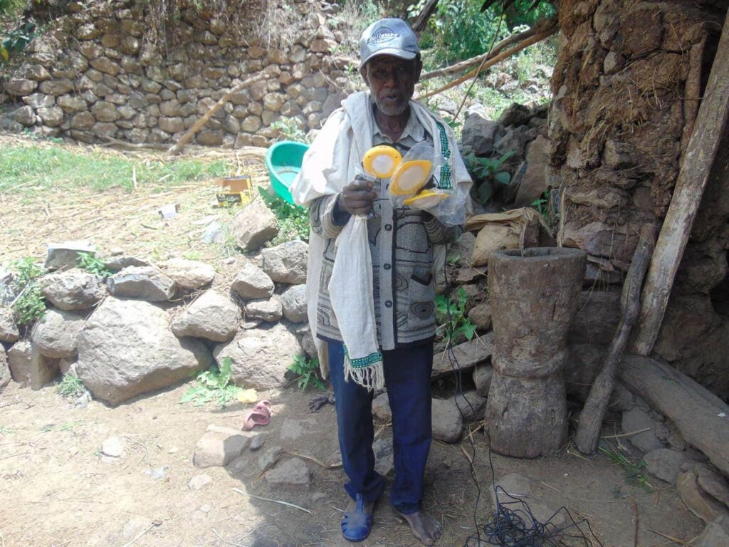 Ein Mann mit gelben Solarlampen in den Händen vor einem Steinhaus