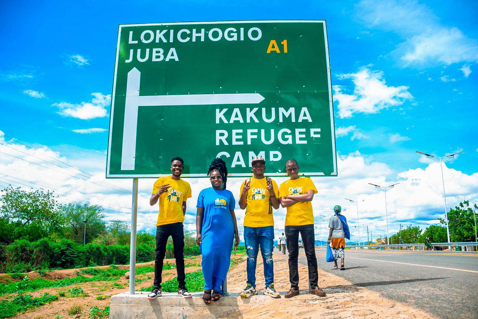 Solar Mtaani Mitarbeitende vor Strassenschild Kakuma Refugee Camp