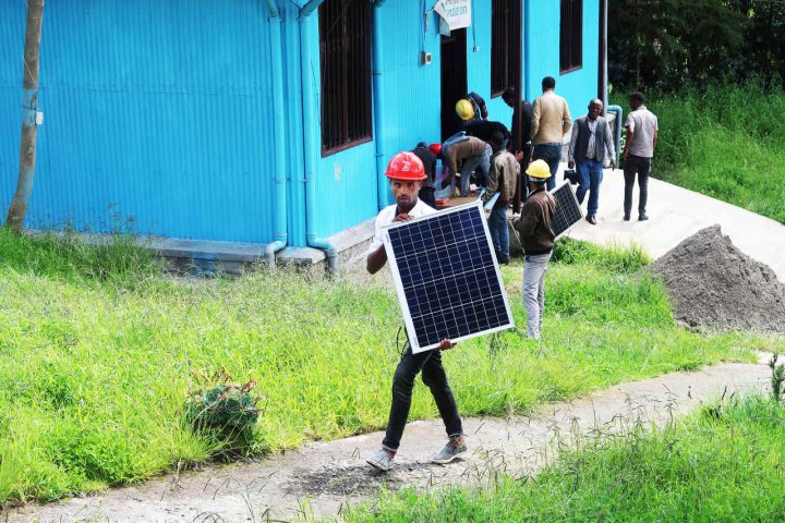 Ein angehender Solartechniker mit rotem Helm trägt ein Solarpanel